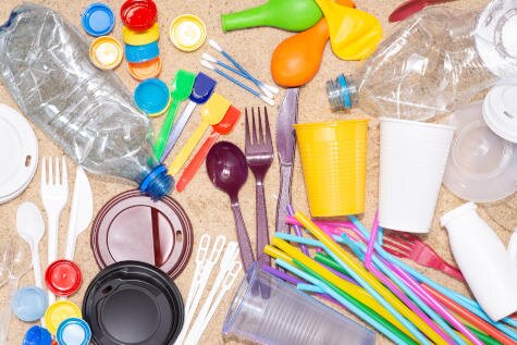 Verschiedene Einweg-Plastikartikel, darunter Flaschen, Becher, Besteck und Strohhalme, auf einem hellen Untergrund