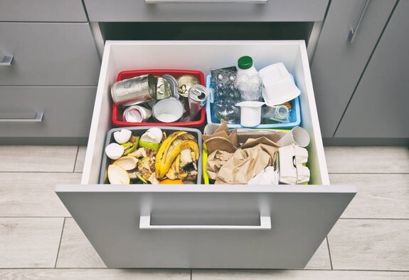 Geöffnete Küchenschublade mit vier Müllbehältern, sortiert nach Papier, Plastik, Dosen und Biomüll